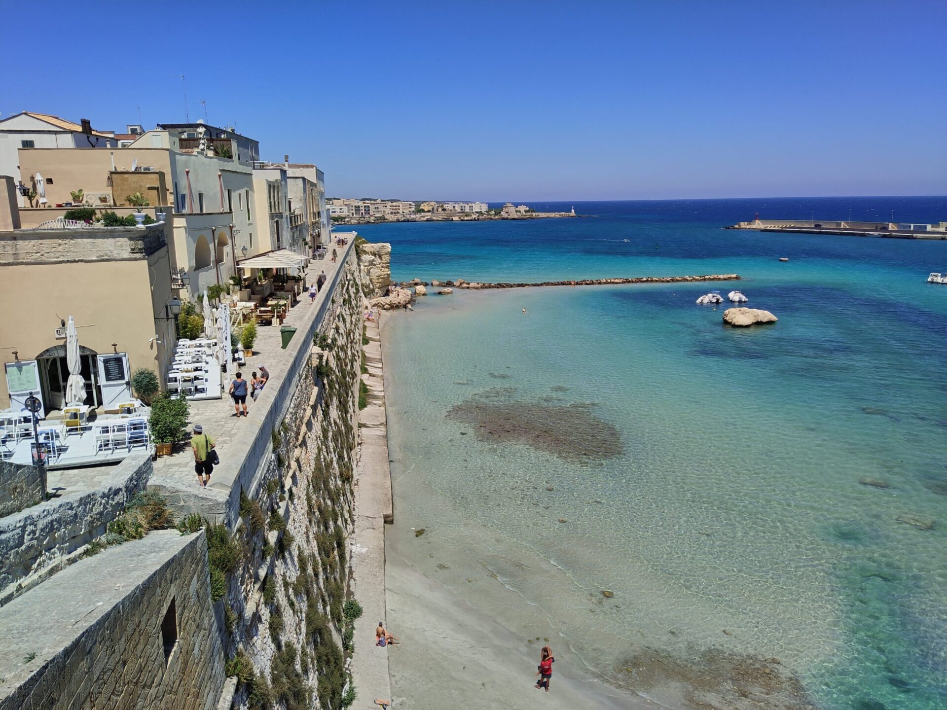 Otranto city walls and harbor with crystal clear turquoise water and traditional fishing boats