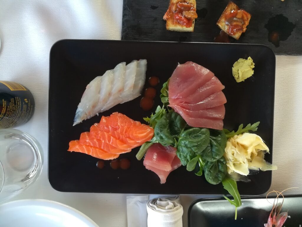 A gourmet plate of fresh Italian seafood cruditè featuring red prawns, langoustines, mussels, and clams, served with lemon and a glass of Rosé wine at Il Vecchio Molo restaurant in San Foca, Puglia.